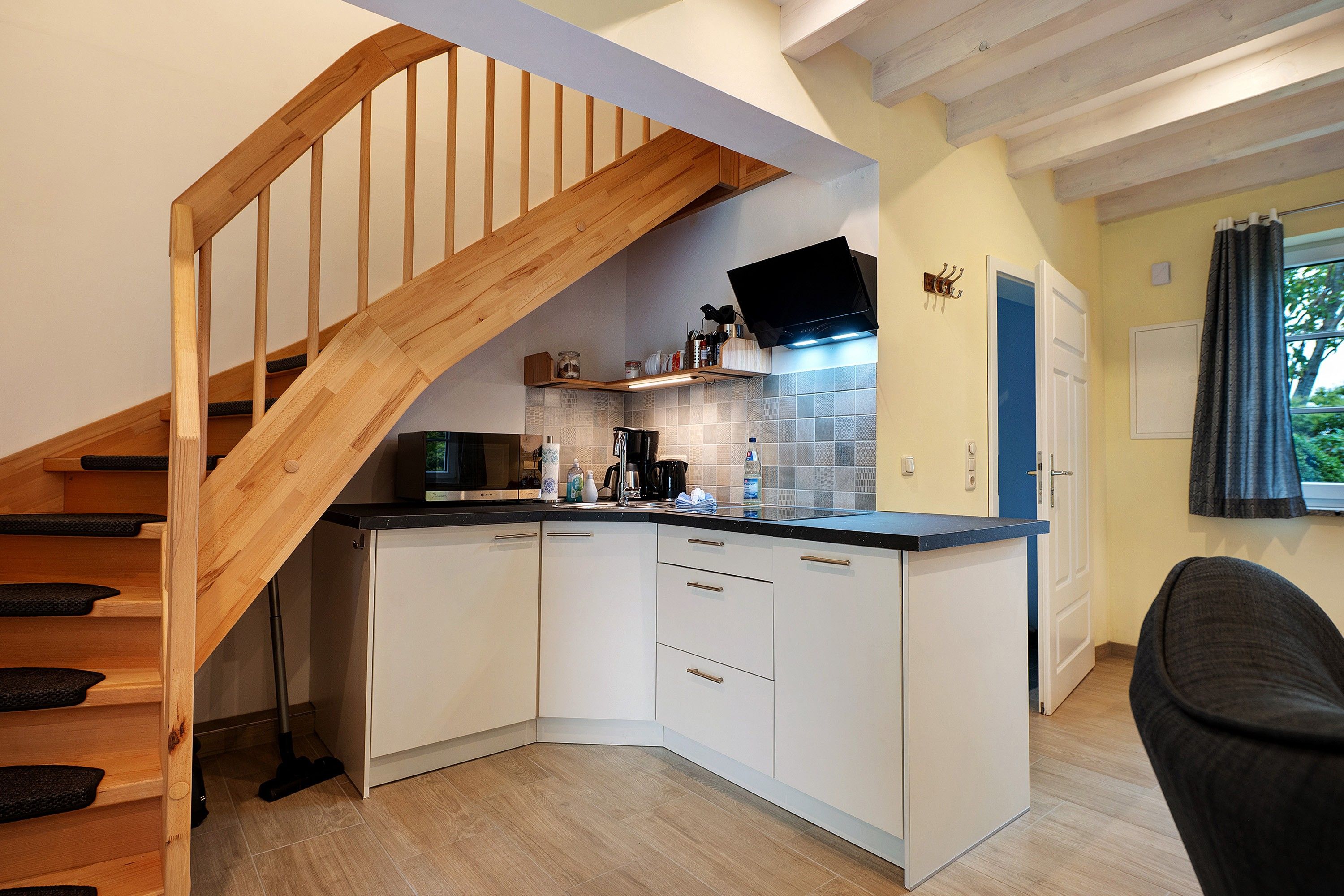 Eine Küche mit weißen Schränken, einer Holztreppe und einer schwarzen Arbeitsplatte.
