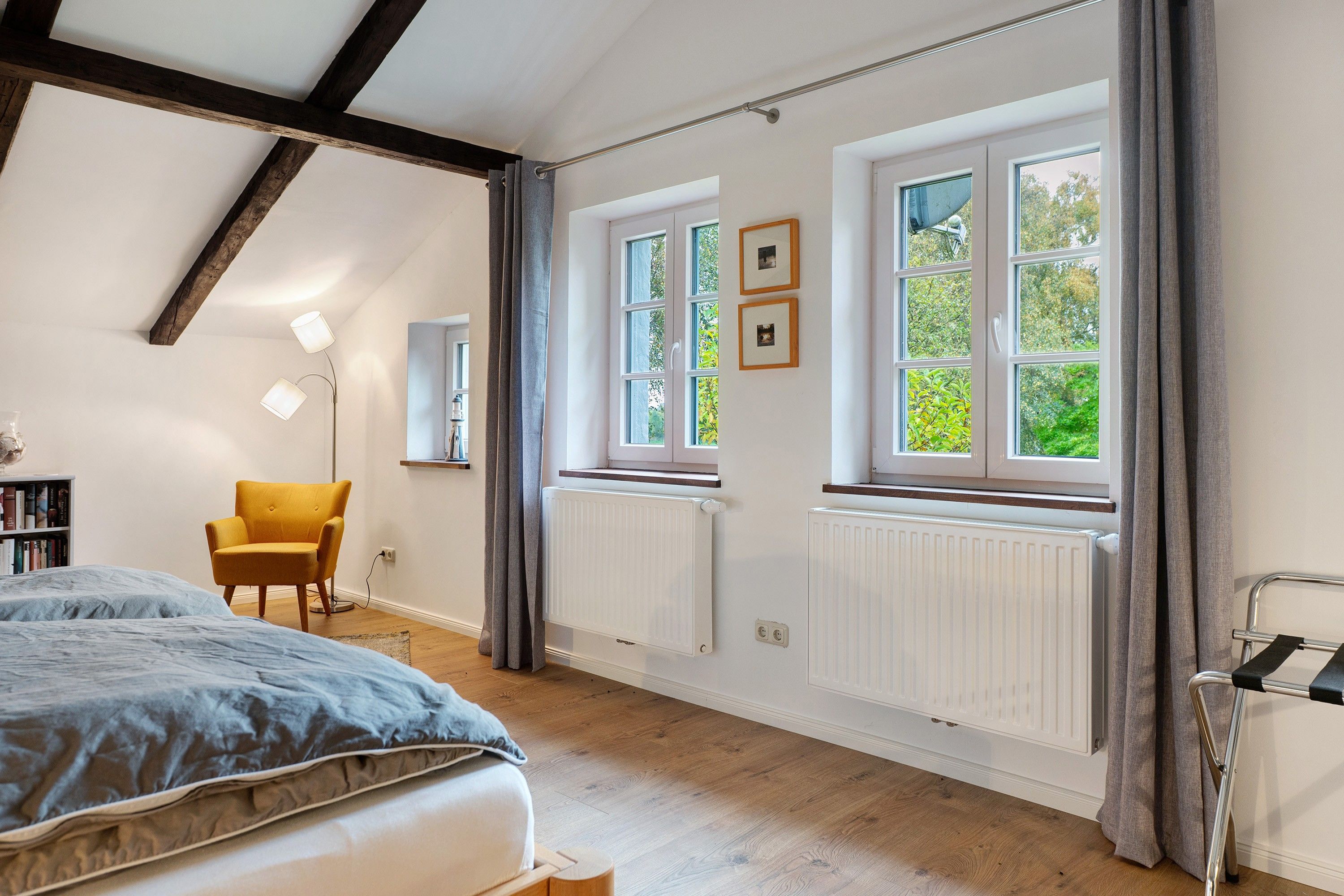 Ein Schlafzimmer mit einem Bett, einem Sessel, einem Heizkörper und einem fenster mit Vorhängen.