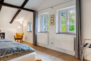 Un dormitorio con cama, una silla, un radiador y una ventana con cortinas.