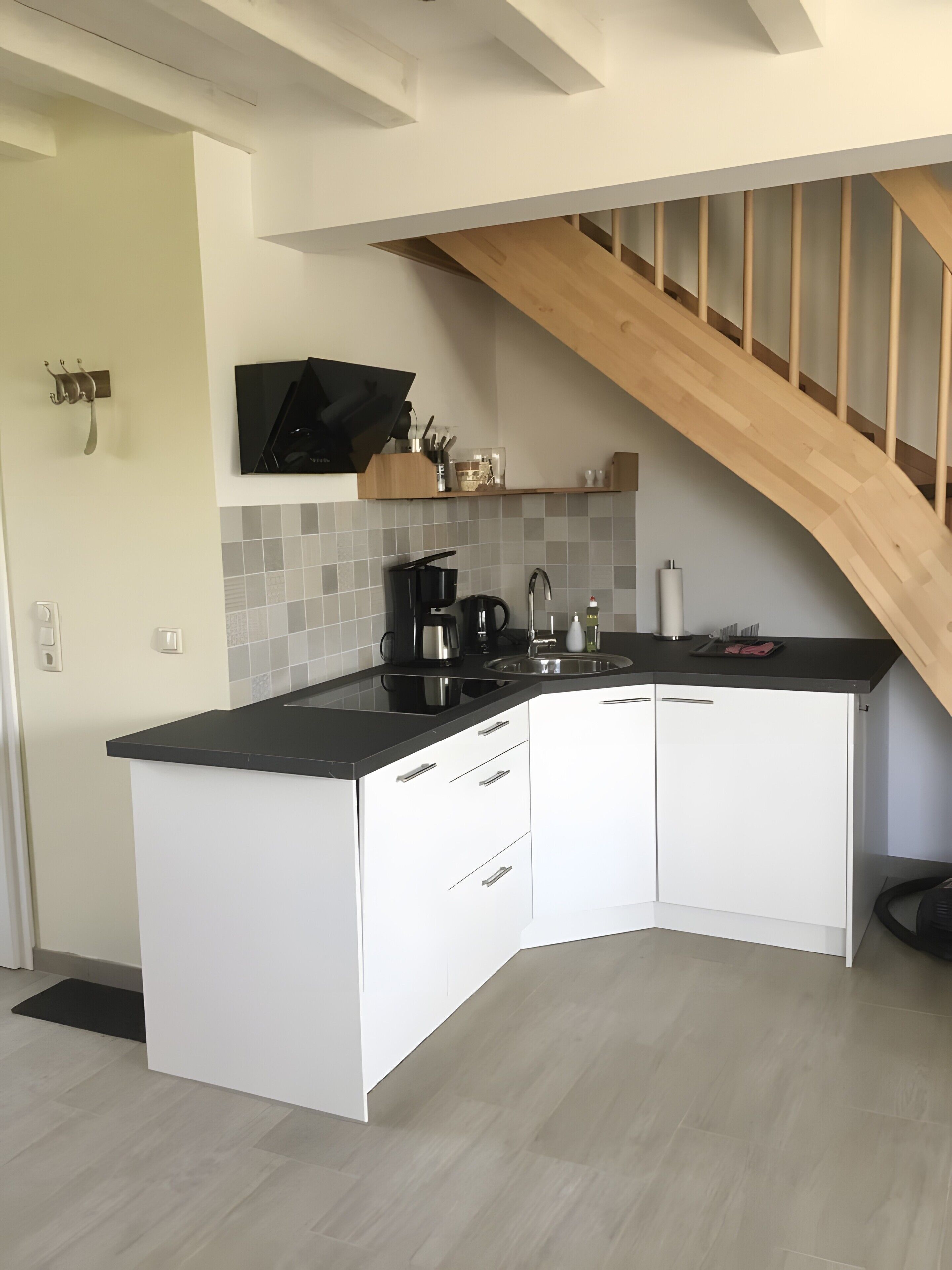 Eine moderne Küche mit schwarzer Arbeitsplatte, weißen Schränken und einer Holztreppe.