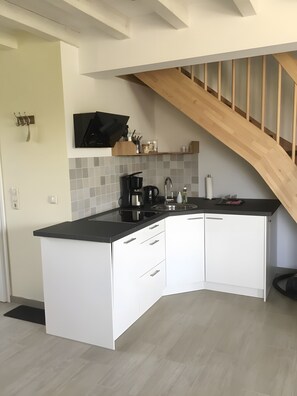 Een moderne keuken met een zwart aanrecht, witte kasten en een houten trap.