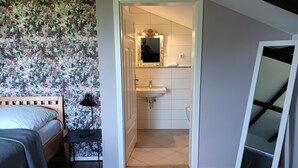 Um quarto com uma cama, mesa de cabeceira e criado-mudo com abajur.