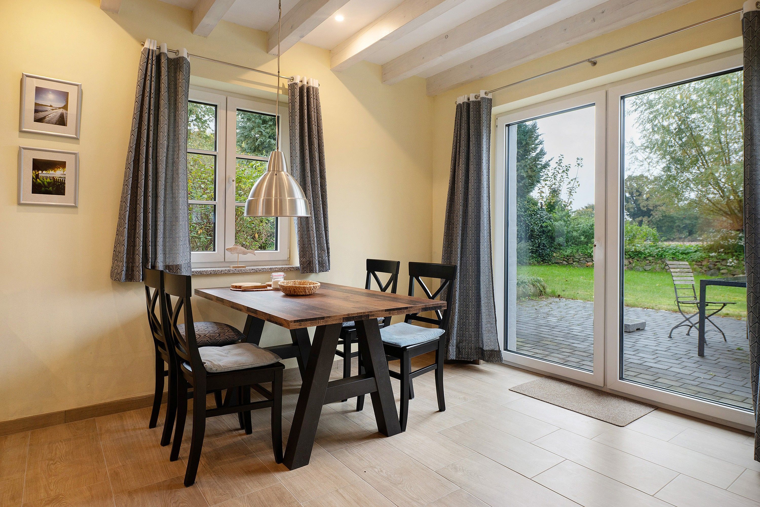 Un comedor con una mesa y sillas de madera, una lámpara colgante y vistas a un jardín a través de un ventanal.