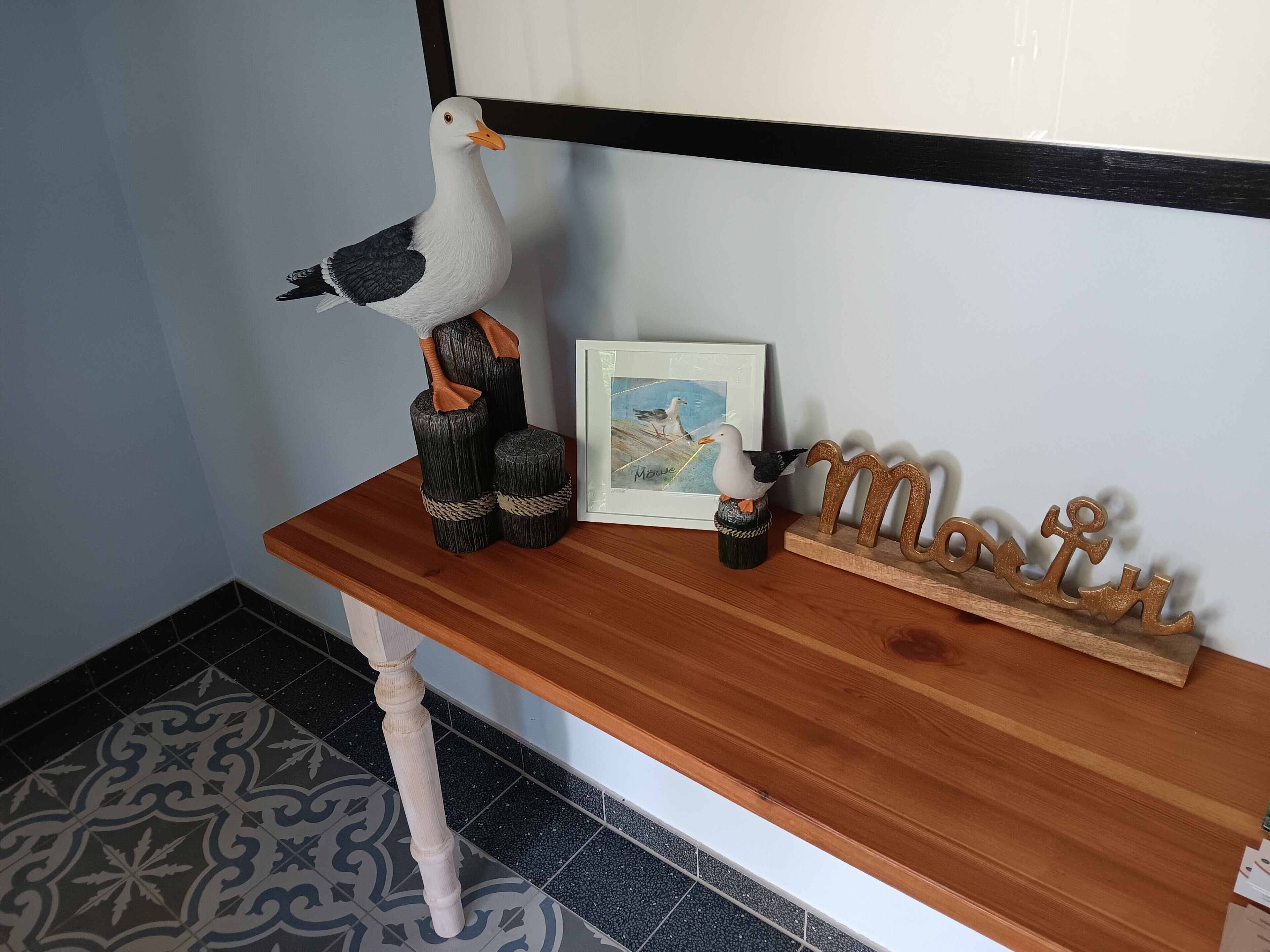 Una mesa de madera con un cuadro enmarco, una escultura decorativa de un pájaro y un letrero de madera con letras.