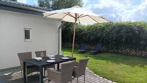 Um pátio externo com mesa posta para refeições, rodeado por cadeiras de vime e um guarda-sol para proteção.