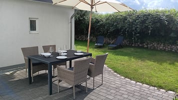 Eine Terrasse im Freien mit einem Esstisch, umgeben von Korbstühlen und einem Sonnenschirm, der Schatten spendet.
