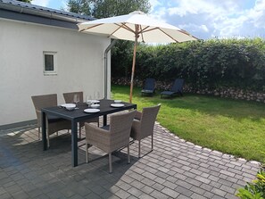 Eine Terrasse im Freien mit einem Esstisch, umgeben von Korbstühlen und einem Sonnenschirm, der Schatten spendet.