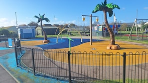 A playground with safety zones, palm trees, and a fenced area. - Mkrj Premium - Parkdean Camber Sands - (Rye)
