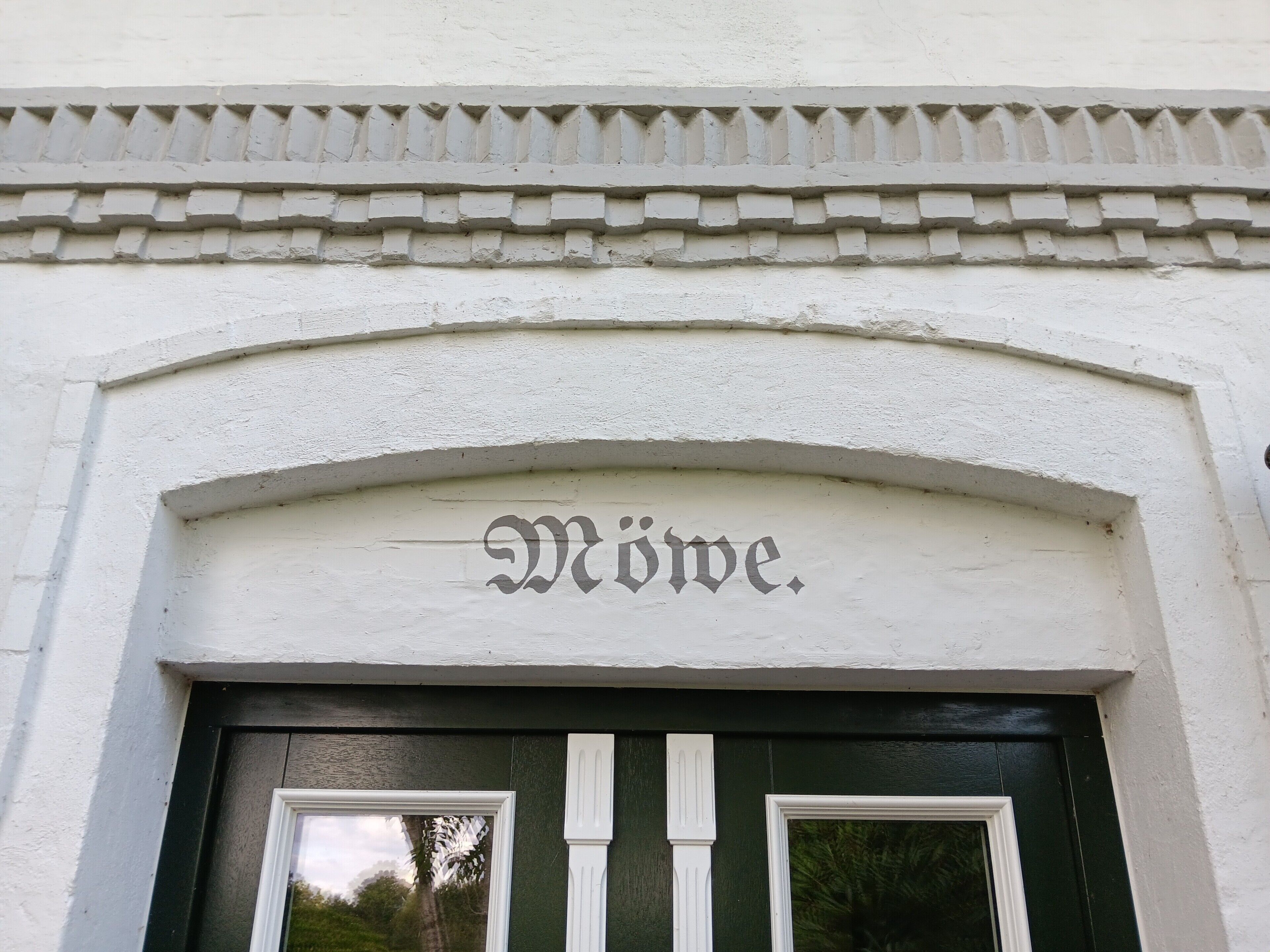 A building entrance with a white facade, a decorative cornice, and the word 'Möve.'