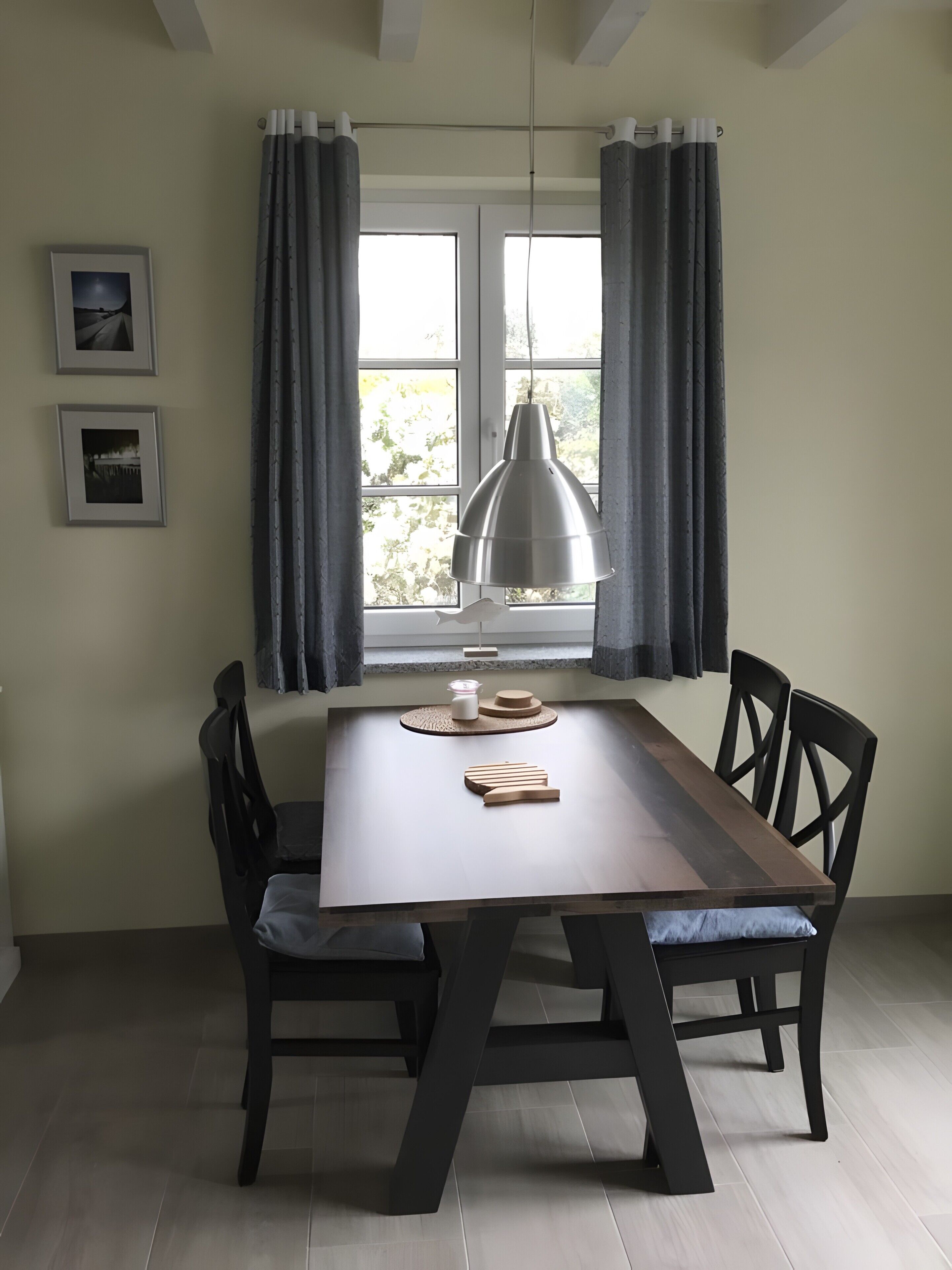 Un coin repas avec une table en bois, quatre chaises, un luminaire suspendu et une fenêtre avec des rideaux.