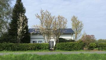 Ein zweigeschossiges Haus mit dunklem Dach, umgeben von gepflegten Hecken und blühenden Bäumen.