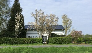 Ein zweigeschossiges Haus mit dunklem Dach, umgeben von gepflegten Hecken und blühenden Bäumen.