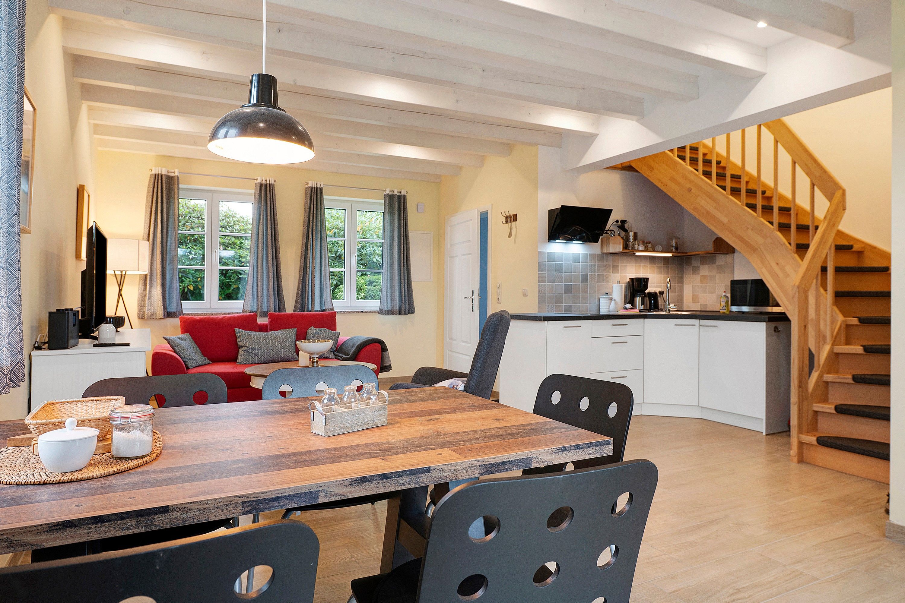 A modern kitchen with white cabinets, a wooden staircase, and a dining area with a wooden table and chairs.
