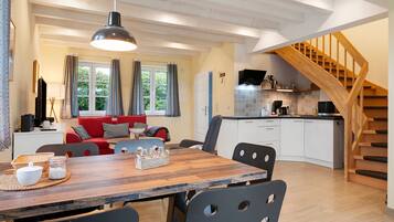 A modern kitchen with white cabinets, a wooden staircase, and a dining area with a wooden table and chairs.
