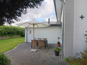 Eine Terrasse im Freien mit Tisch, Stühlen, einem großen Sonnenschirm und Blumentöpfen.