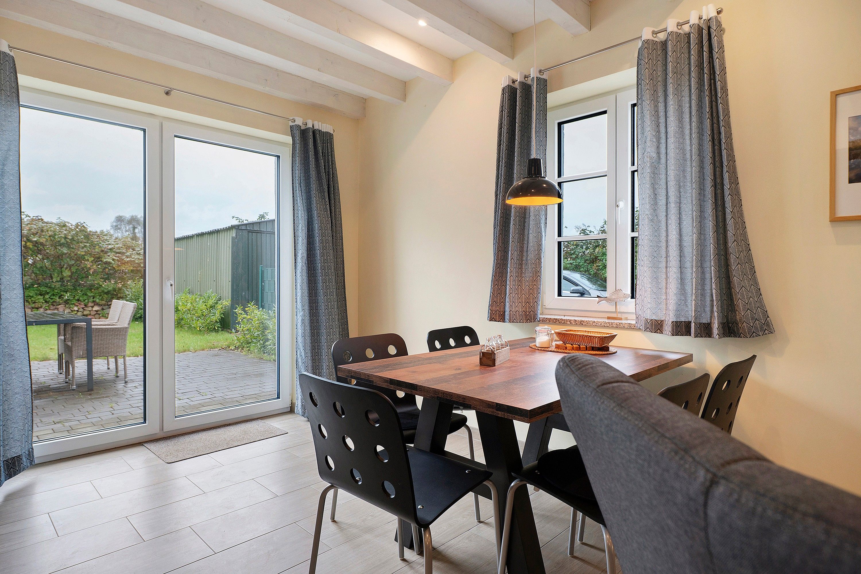 Un comedor con mesa y sillas, una ventana con cortinas y vistas al exterior.