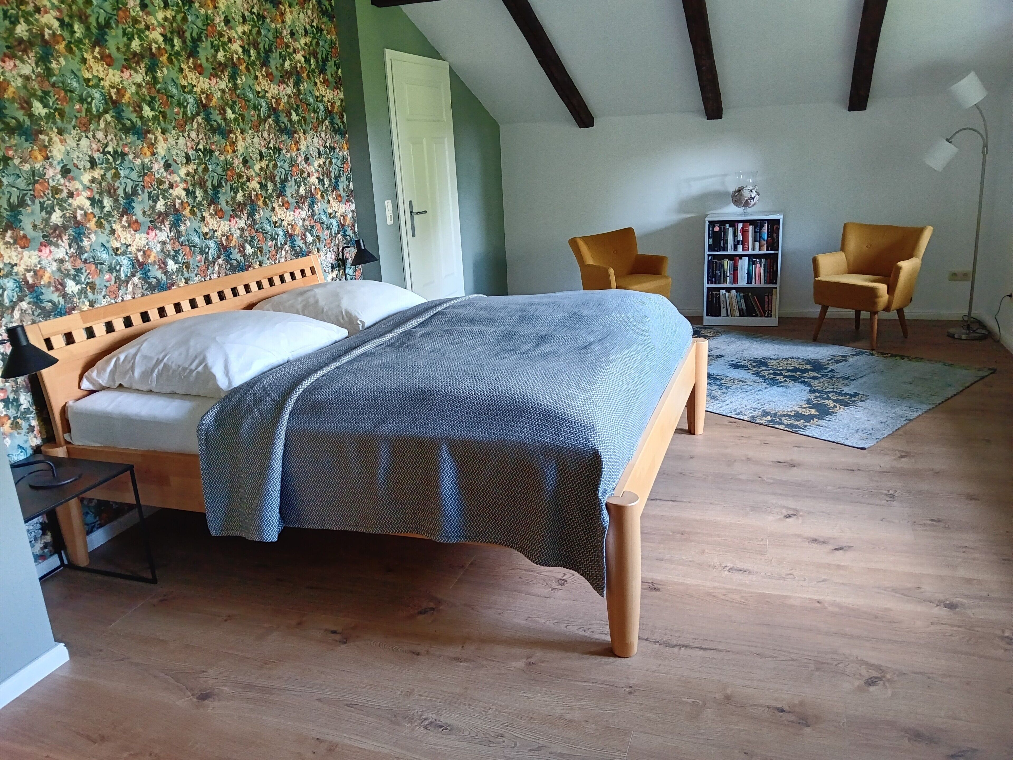 Une chambre à coucher avec un lit en bois, une bibliothèque, deux chaises et un tapis à motifs.