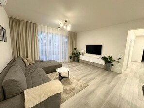 Un salon moderne avec un canapé d’angle, une petite table basse ronde et un téléviseur à écran plat fixé au mur.