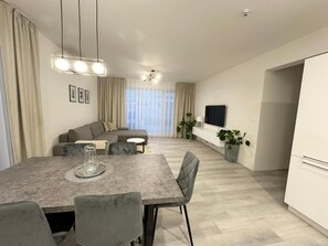 A modern living room with a dining area, a sofa set, a TV, and a kitchen area with a plant. - AC Apartment House with Jacuzzi, 9A (Senec)