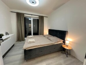 Een moderne slaapkamer met een bed, nachtkastje en uitzicht op een balkon.