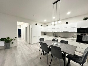 A modern kitchen with white cabinets, a dining table with chairs, and a built-in oven.