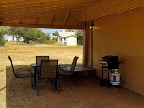 Une terrasse extérieure couverte, équipée d’une table et de chaises, d’un barbecue et d’une bouteille de propane.
