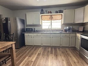 A kitchen with a wooden floor, white cabinets, a refrigerator, a microwave, a sink, and a coffee maker.