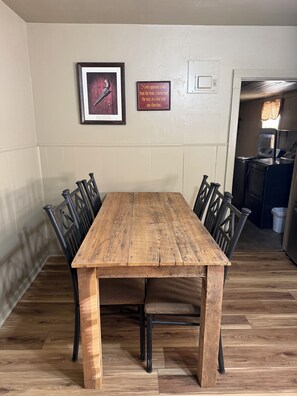 Une table à manger avec des chaises, un tableau encadré et une enseigne fixée au mur, dans une pièce dont le sol est recouvert de parquet.