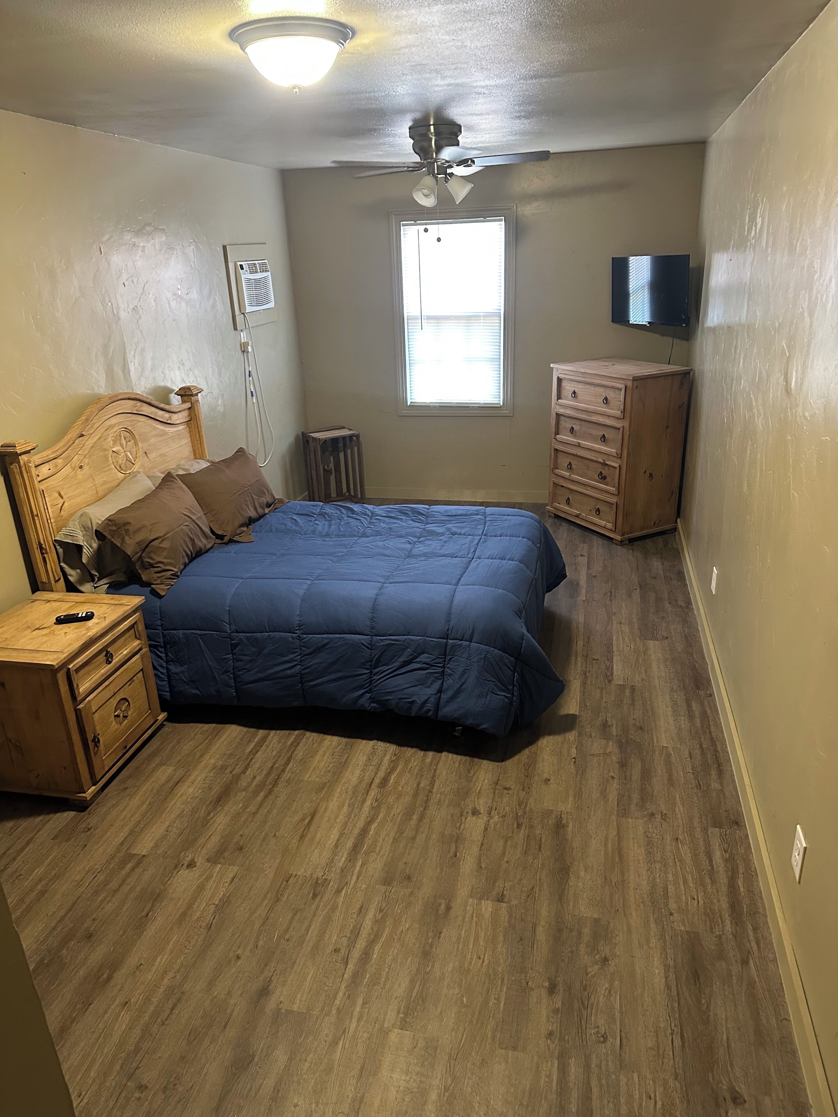 A bedroom with a bed, wooden nightstand, dresser, ceiling fan, and a window.