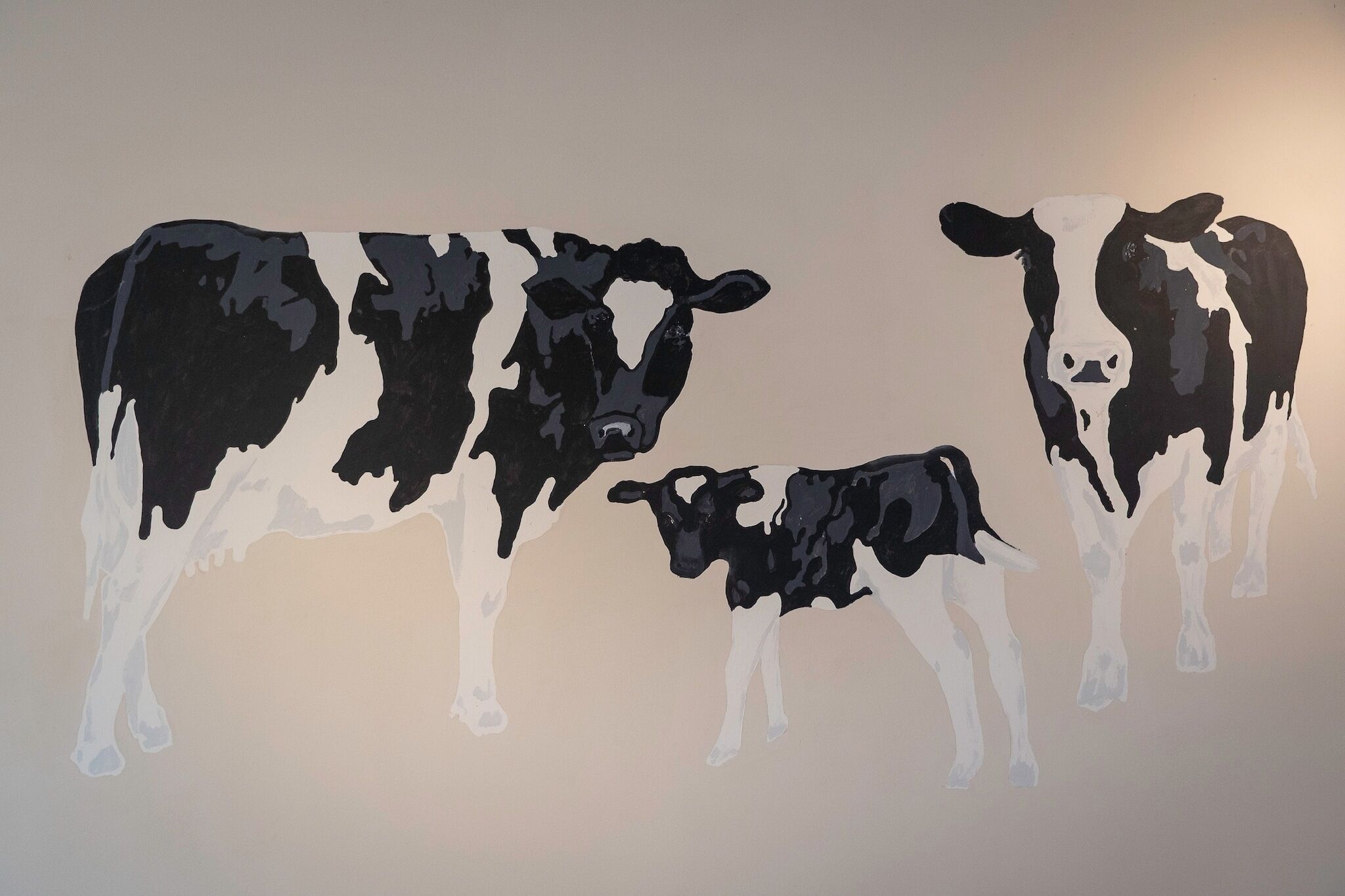 A wall with a painting of two cows, one larger and one smaller, both in black and white.