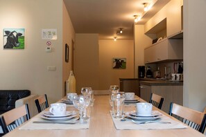 Un comedor con una mesa dispuesta para seis personas, sillas, una cocina con electrodomésticos y obras de arte en las paredes.