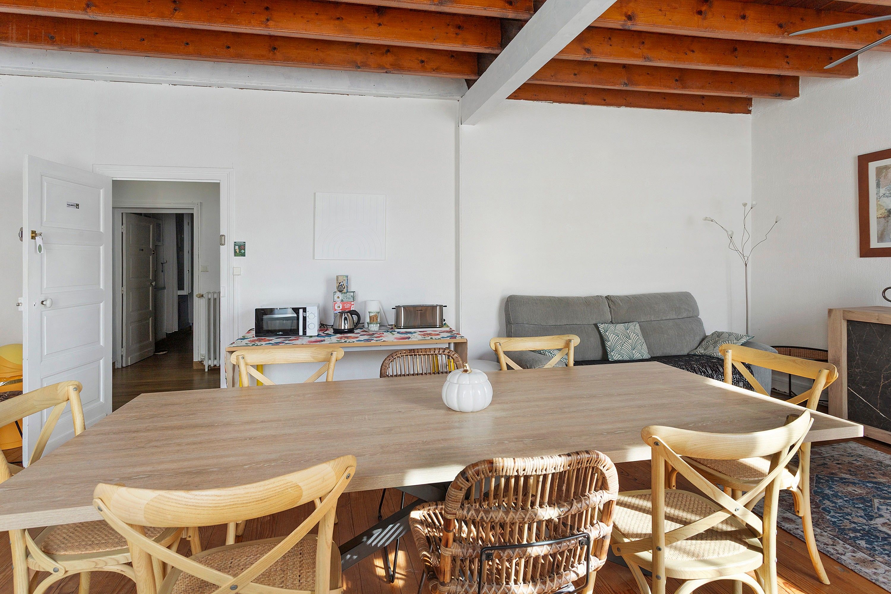 Un comedor con una mesa de madera, sillas de mimbre y una cocina al fondo.