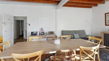 Un comedor con una mesa de madera, sillas de mimbre y una cocina al fondo.