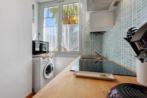 A compact kitchen with a washing machine, a microwave, and a sink with a tiled backsplash. - “Gîte de l'isard” Apartment: Mountain View, Private Garden, Wi-Fi (Pierrefitte-Nestalas)
