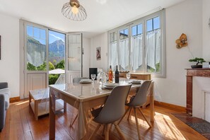 Zona pranzo con tavolo in legno, sedie e vista sulle montagne attraverso ampie finestre.
