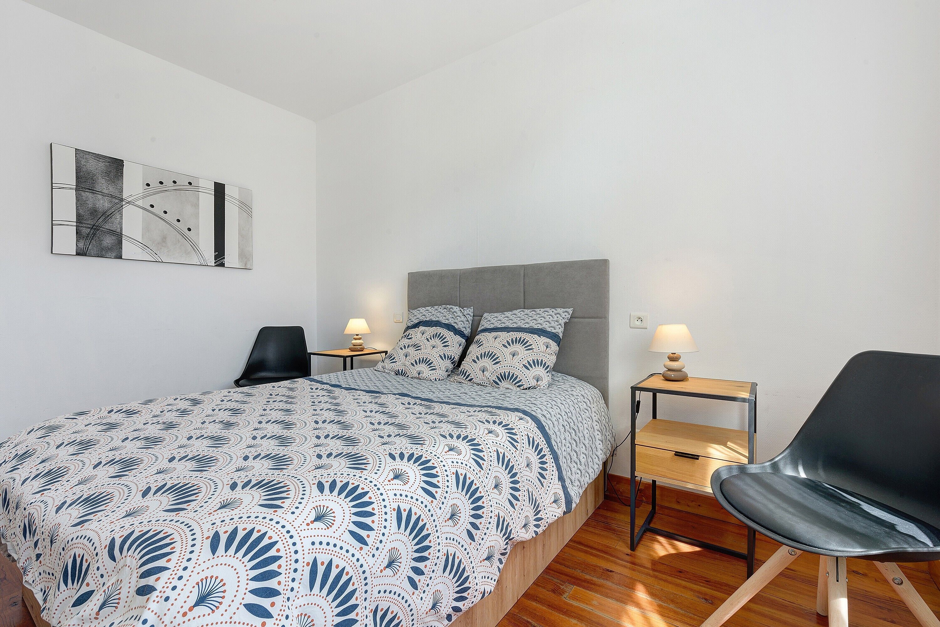 A bedroom with a bed, two bedside tables with lamps, a chair, and a wall art piece.