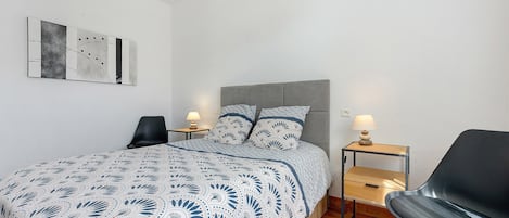 A bedroom with a bed, two bedside tables with lamps, a chair, and a wall art piece.