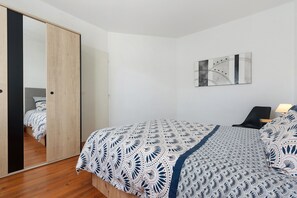 Ein Schlafzimmer mit einem Bett, einem Sessel, einem Schreibtisch, einem Spiegel und einem Wandbild.
