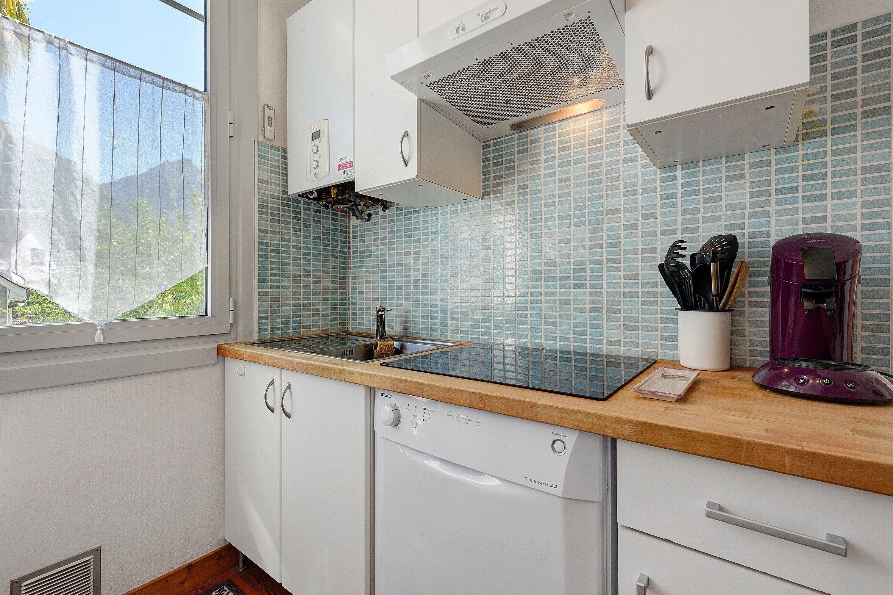 Una cocina con armarios blancos, encimera de madera, estufa integrada y ventana con vistas a la vegetación.