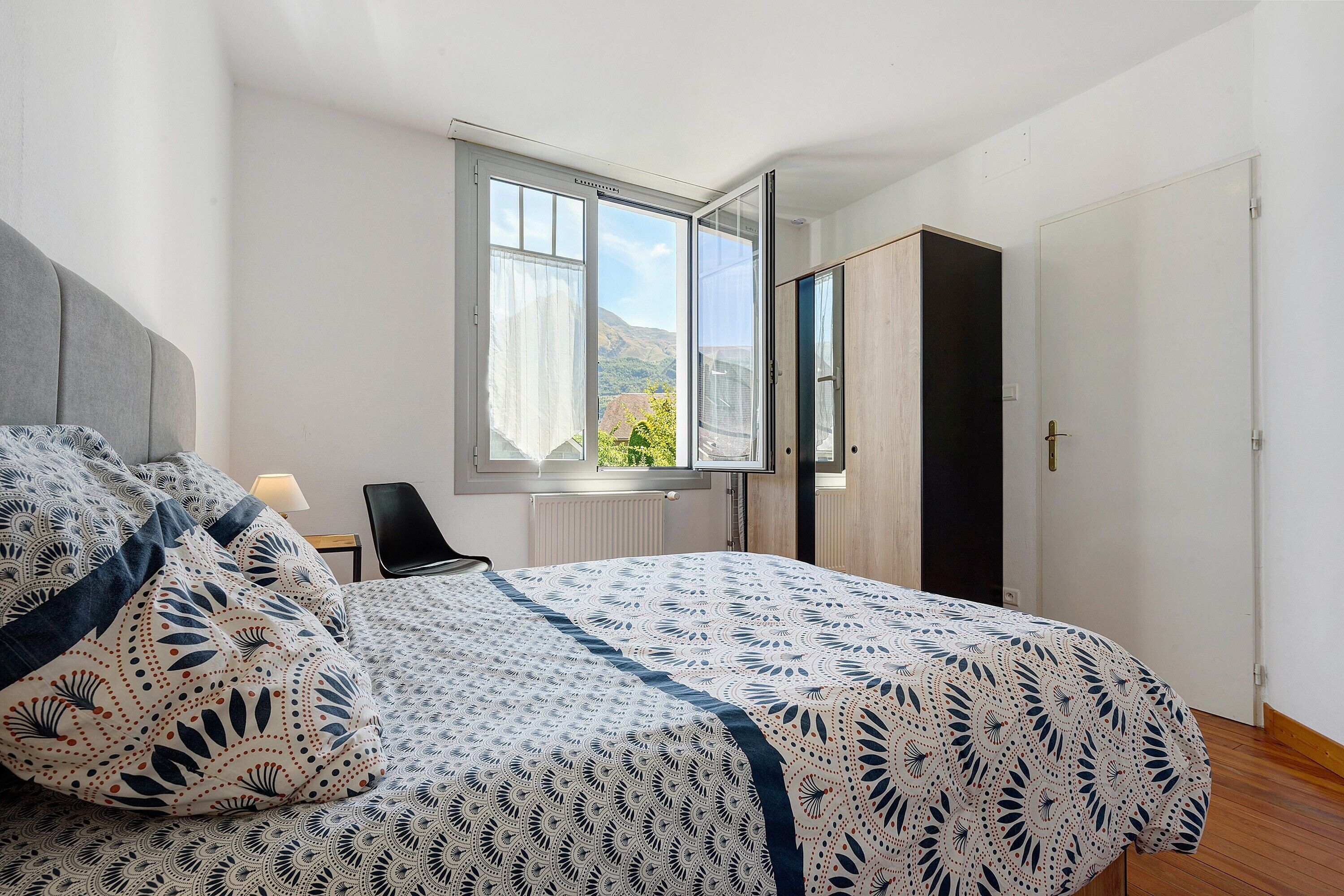 Een slaapkamer met een bed, een stoel, een raam met uitzicht en een kledingkast.