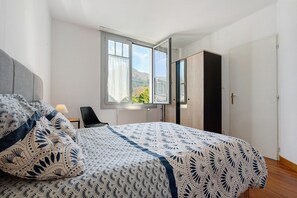 Ein Schlafzimmer mit Bett, Sessel, Fenster und Kleiderschrank.