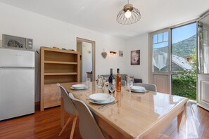 Eine moderne Küche mit Esstisch für vier Personen, einem Kühlschrank und Blick auf eine gebirgige Landschaft durch ein großes Fenster.