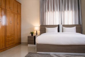 Une chambre à coucher avec un grand lit, une armoire en bois, une table de chevet avec une lampe et des rideaux.