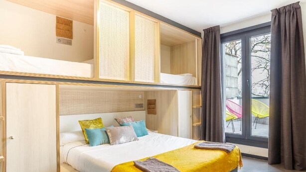 A hotel room with a bunk bed, a large window with curtains, and a view of outdoor chairs. - Cats San Sebastian (San Sebastian)