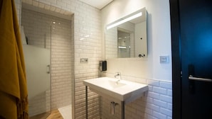 A modern bathroom with a white-tiled shower, a white sink with a mirror, and a towel rack. - Cats San Sebastian (San Sebastian)
