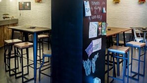 A modern interior with a central pillar featuring a chalkboard with text, surrounded by tables and chairs. - Cats San Sebastian (San Sebastian)