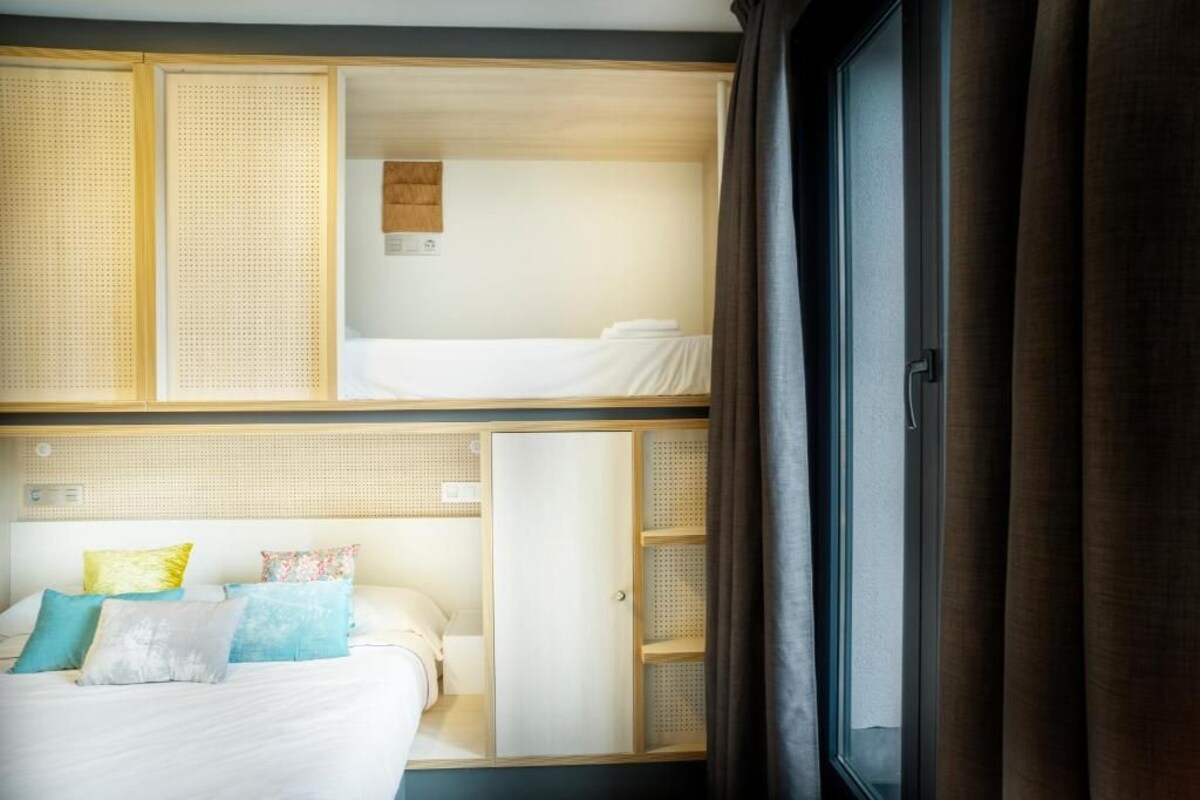 A hotel room with a bunk bed, a separate bed, and a wardrobe with a mirror.