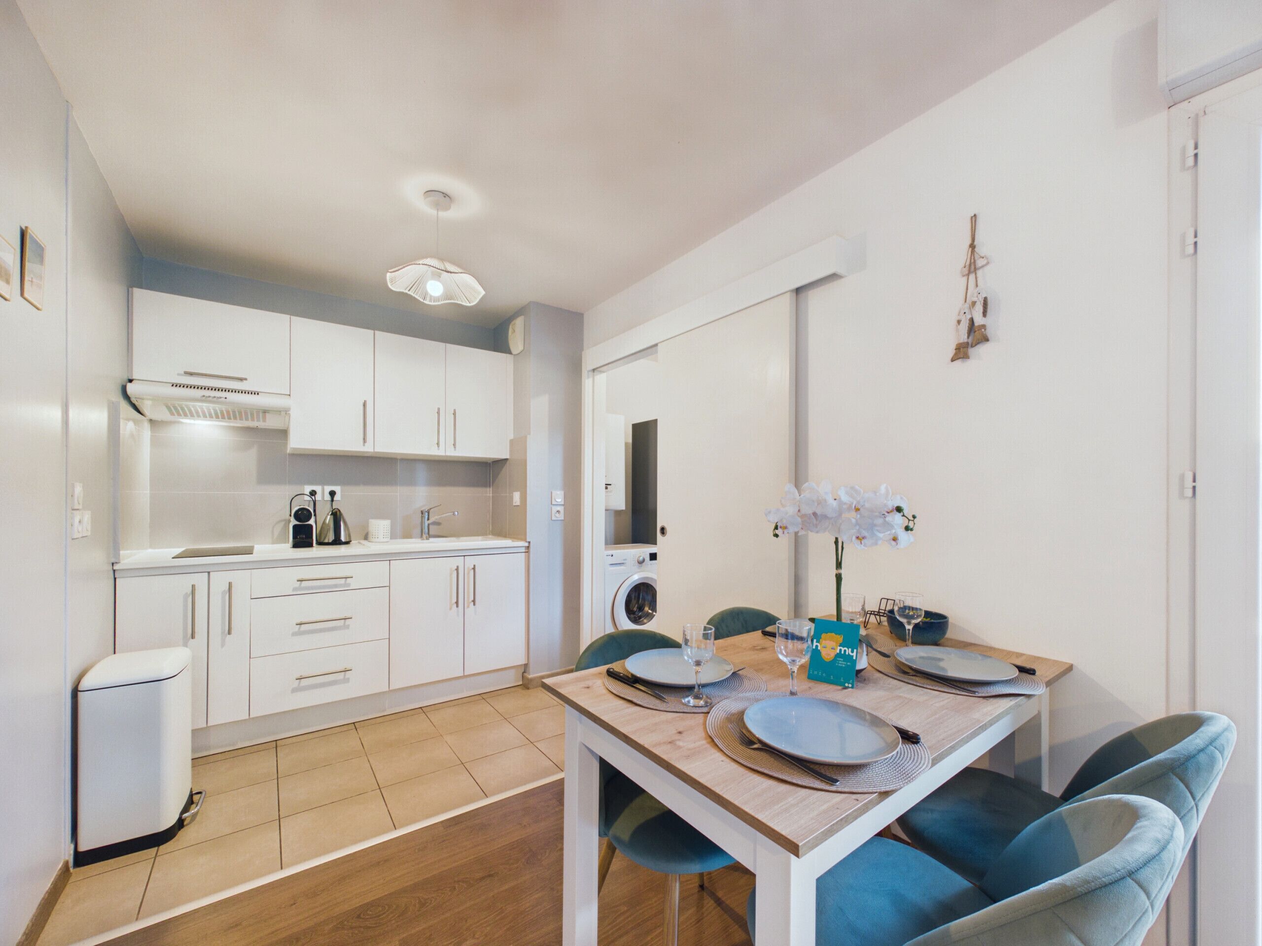 Une cuisine moderne avec des meubles blancs, un four encastré et un coin repas agrémenté d’une table en bois mise pour deux personnes.