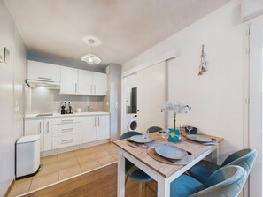 A modern kitchen with white cabinets, a built-in oven, and a dining area with a wooden table set for two. - Apartment for 2 adults/2 kids near Grande Plage (Les Sables-d´Olonne)