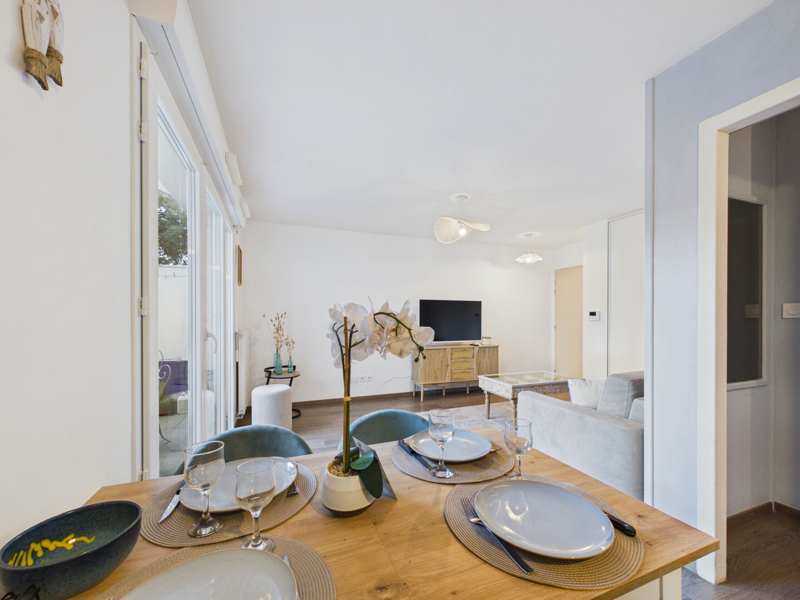 A dining area with a wooden table set for four, a television in the background, and a modern interior design.